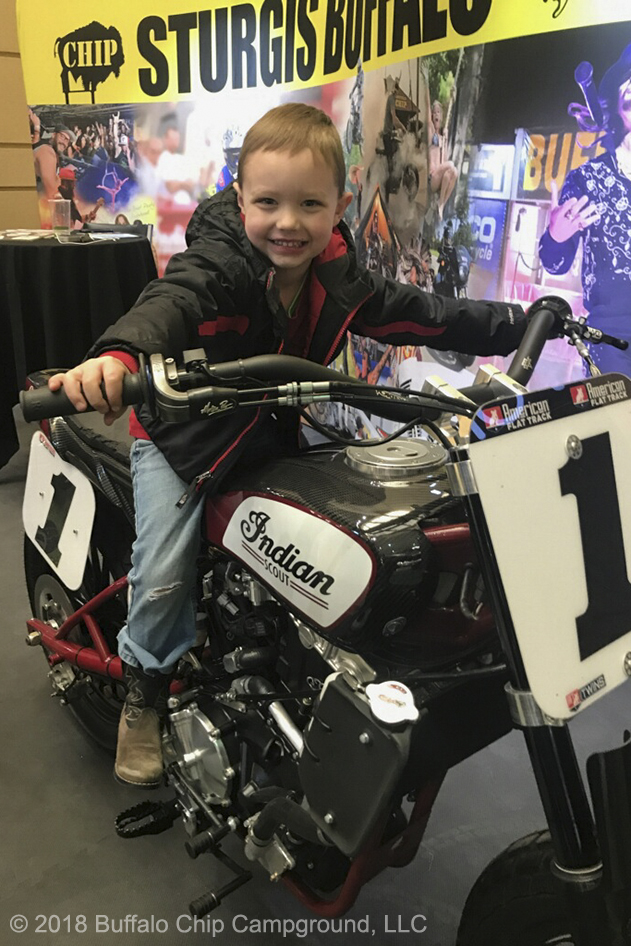 A young show attendee smiles atop the Indian FTR750 in the Sturgis Buffalo Chip display